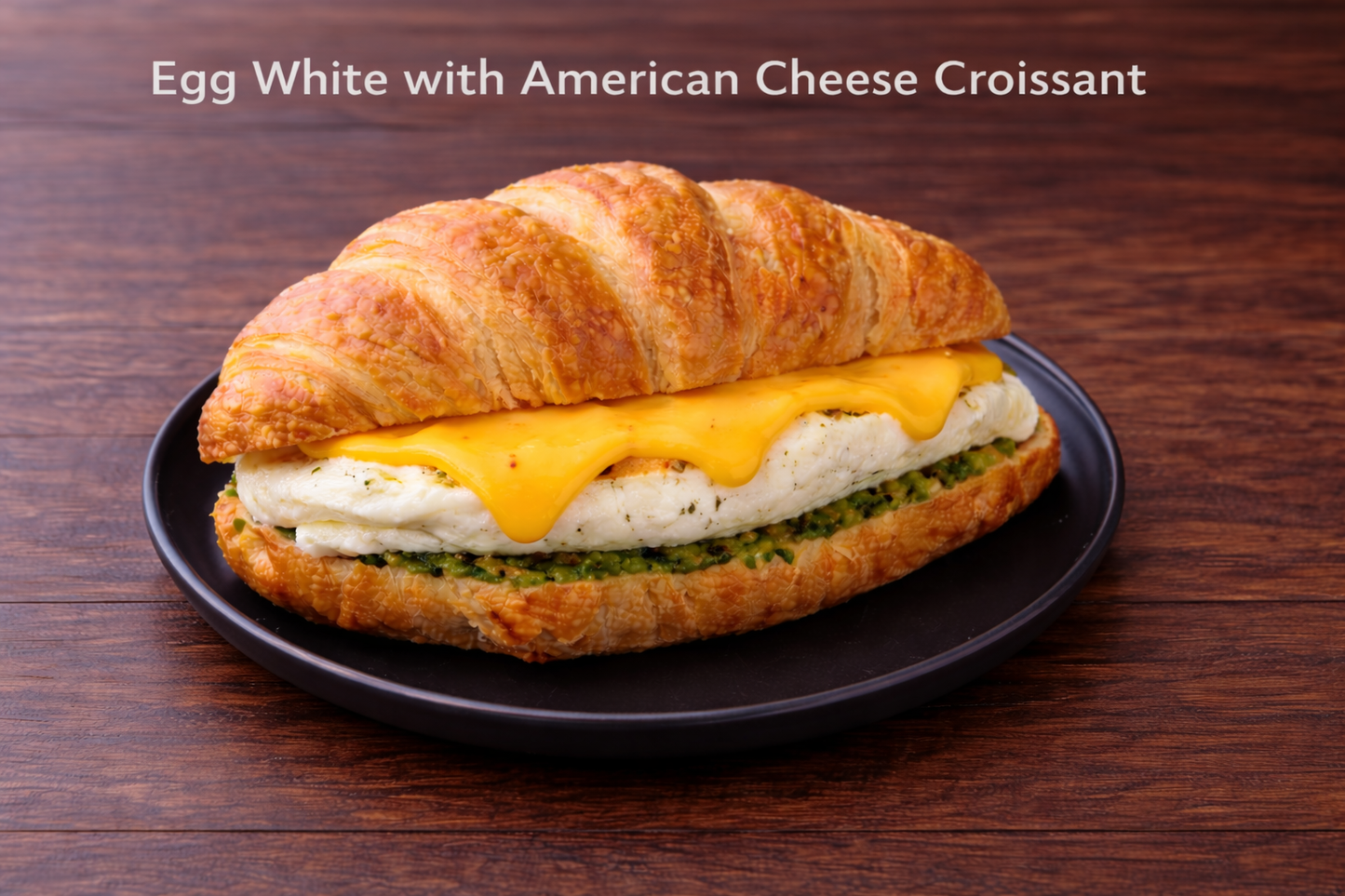 Croissant sandwich with egg white and American cheese on a dark plate against a wooden background