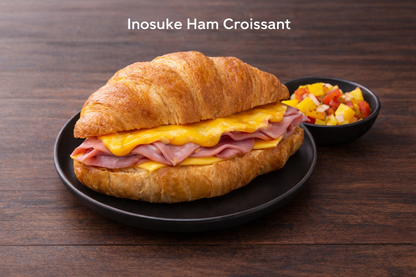 Inosuke Ham Croissant on a black plate with a side of fruit salad on a wooden table.